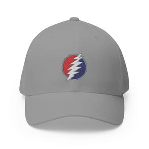 May include: A gray baseball cap featuring an embroidered emblem. The emblem is a white lightning bolt design, set within a red and blue circle. The cap has a curved brim and a structured fit, suitable for casual wear.