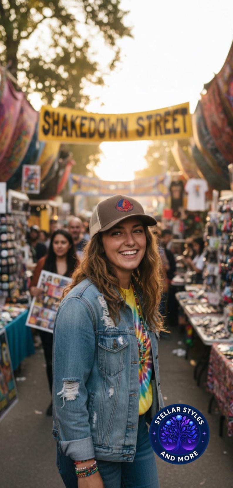 May include: A person smiling, wearing a brown and beige trucker cap with a patch, a denim jacket, and a tie-dye shirt. The background shows a market scene and a banner reading "Shakedown Street".