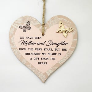 Puede incluir: Un letrero de madera en forma de corazón rosa y beige con un diseño de mariposa y el texto "We have been Mother and Daughter from the very start, but the friendship we share is a gift from the heart."