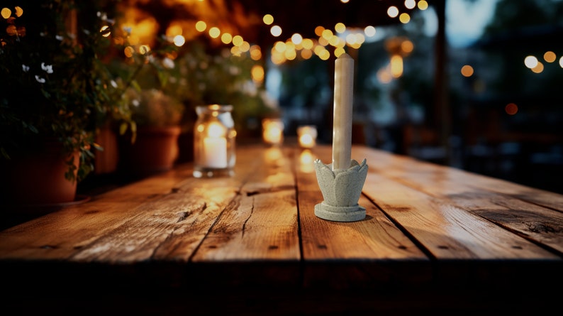 May include: A white candle sits in a light blue ceramic candle holder shaped like a flower. The candle holder is on a wooden table with a blurred background of lights and plants.