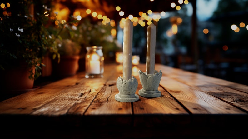 May include: Two white candles in simple, light blue, flower-shaped candle holders on a wooden table. The candles are lit and the table is in a dimly lit setting.