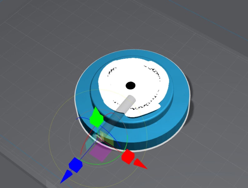 May include: A blue and white circular object with a white center and a black dot in the center. The object is on a gray surface with a grid pattern.