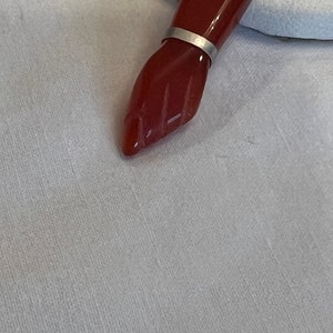 May include: A red carnelian gemstone pendant with a silver setting. The pendant is shaped like a hand with the fingers closed.