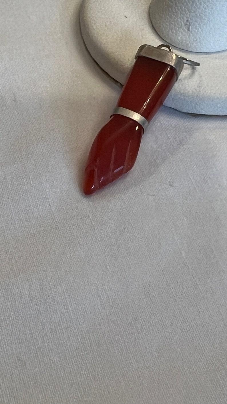 May include: A red carnelian gemstone pendant with a silver setting. The pendant is shaped like a hand with the fingers closed.