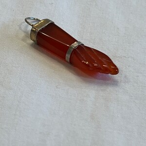 May include: A red carnelian gemstone hand pendant with a silver setting. The pendant is carved in the shape of a hand with a closed fist.
