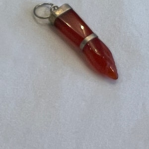 May include: A red carnelian gemstone pendant with a silver setting. The pendant is shaped like a teardrop and has a pointed tip.