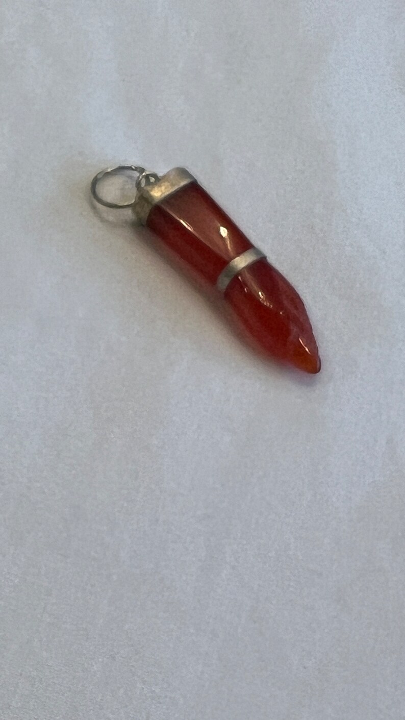 May include: A red carnelian gemstone pendant with a silver setting. The pendant is shaped like a teardrop and has a pointed tip.
