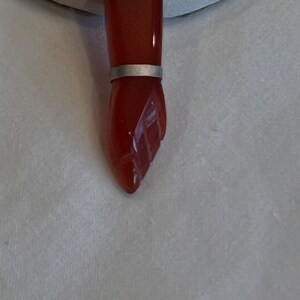 May include: A carved carnelian stone hand pendant with silver accents. The pendant is a detailed carving of a hand with a silver band around the wrist.
