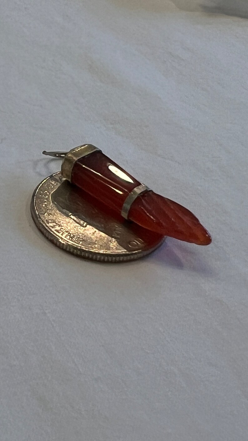 May include: A red carnelian gemstone pendant with silver accents. The pendant is shaped like a tooth and is about 1 inch long.