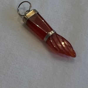 May include: A red carnelian gemstone pendant with a silver setting. The pendant is shaped like a hand with a pointed finger.