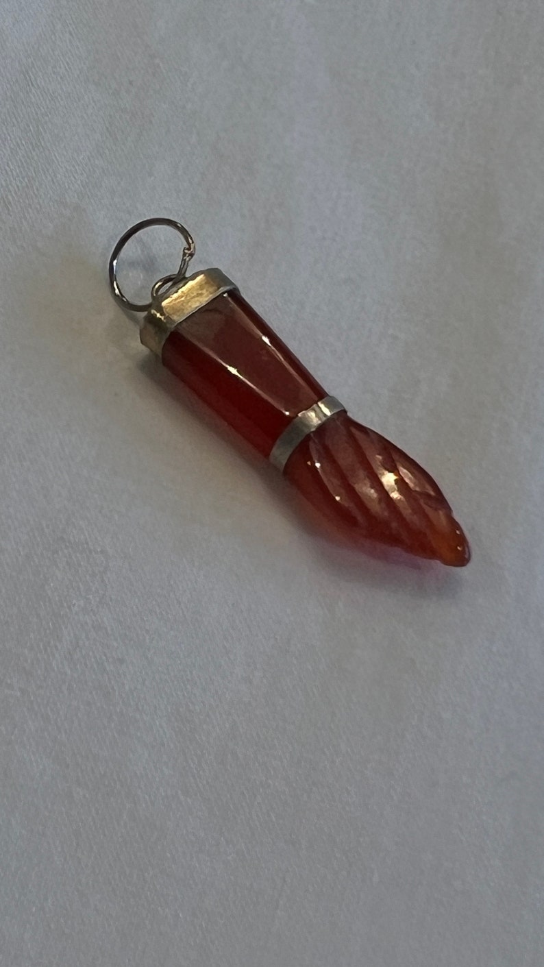 May include: A red carnelian gemstone pendant with a silver setting. The pendant is shaped like a hand with a pointed finger.