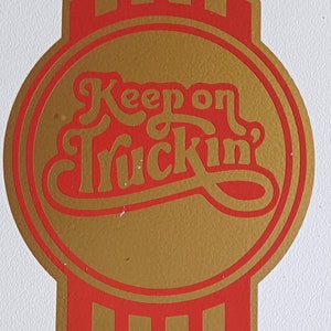 May include: A gold and red logo with the text "Keep on Truckin'" in a stylised font. The logo is in the shape of a stylised truck grill.