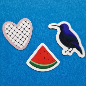 Puede incluir: Tres pegatinas coloridas sobre un fondo azul. Un corazón rosa con un patrón de cuadrícula blanco y negro, un pájaro azul con un pico largo y una rebanada de sandía roja.