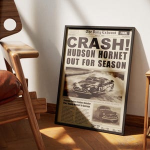 Può includere: Un titolo di giornale vintage che annuncia il "CRASH!" della Hudson Hornet, con una foto in bianco e nero dell'auto in una nuvola di fumo. Il titolo recita "Hudson Hornet Out For Season".