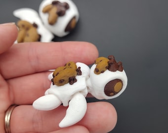May include: White 3D printed figurine of a robot with brown chocolate chip cookies on its back. The robot has a brown eye and white arms and legs.