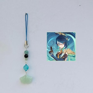 May include: A blue and green phone charm with a jade green fan charm, black and green beads, and a blue string. The charm features a cartoon image of a woman with blue hair and glasses.