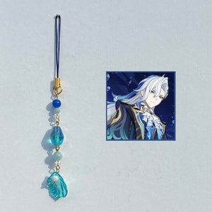 May include: A blue and white beaded phone charm with a crystal pendant. The charm features a blue and white image of a character with white hair and blue eyes.