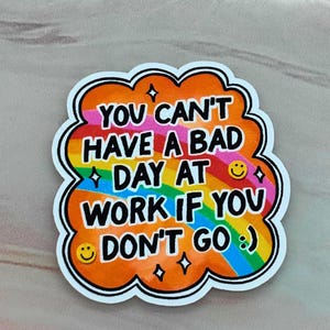 Könnte beinhalten: Ein farbenfroher Aufkleber mit dem Text "YOU CAN'T HAVE A BAD DAY AT WORK IF YOU DON'T GO :)". Der Aufkleber hat ein Regenbogen-Design mit orangefarbenen und weißen Rändern und enthält Smiley-Gesichter und Sternakzente.