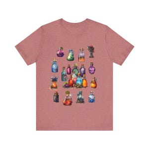 May include: A heather pink t-shirt with a colorful illustration of various potion bottles. The bottles are filled with different colored liquids and have cork stoppers. Some of the bottles have labels with text.