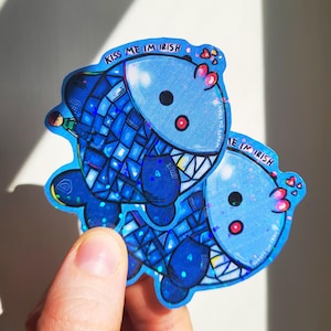May include: Two blue holographic stickers featuring a cartoon character design. The character is a blue fish with a toothy grin and the text "Kiss me I'm Irish" on the sticker.