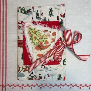 Pode incluir: Uma meia de Natal de tecido vermelho e branco com uma ilustração vintage do Papai Noel carregando uma árvore de Natal. A meia é decorada com renda branca e uma fita vermelha e branca.