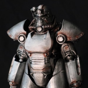 May include: A metallic silver power armor figurine featuring a helmet with a circular visor, a chest plate, and shoulder pauldrons. The suit displays weathered textures with dark brown rust-like accents along the joints and edges of the armor plating.