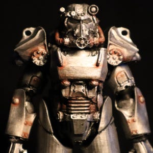 May include: A detailed, metallic silver and rust-coloured power armour figurine. The armour features intricate mechanical details, including a helmet with a respirator and various tubes and rivets. The overall design suggests a post-apocalyptic or science fiction theme.