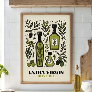 May include: A framed print with a white background and a green and black illustration of olive oil bottles, olive branches, and olives. The text "EXTRA VIRGIN OLIVE OIL" is printed below the illustration.