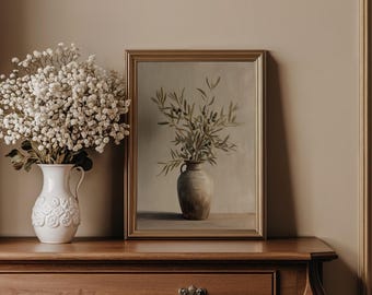May include: A framed wall art print featuring a painting of an olive branch in a ceramic vase, displayed next to a white pitcher filled with white baby's breath flowers. The artwork is set in a gold-toned frame, capturing a still life composition.