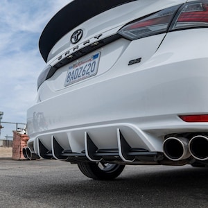 Könnte beinhalten: Ein weißer Toyota Camry mit einem schwarzen Heckspoiler und einem schwarzen Heckdiffusor mit fünf Finnen. Das Auto hat ein kalifornisches Nummernschild mit der Aufschrift "8ADZ620".