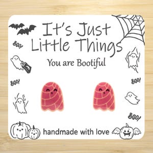May include: A pair of ghost-shaped earrings with a red and pink design, set against a white background with Halloween-themed illustrations and text that reads "It's Just Little Things, You are Bootiful" and "handmade with love".