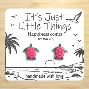 May include: A pair of pink and green turtle stud earrings on a white card with the text "It's Just Little Things Happiness comes in waves handmade with love".