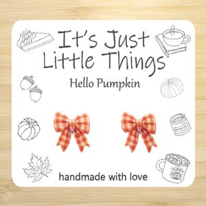 May include: A white card with the text "It's Just Little Things" and "Hello Pumpkin". Two orange and white gingham bow earrings are featured. The card also includes sketched drawings of fall-themed items.
