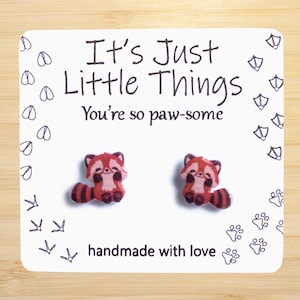 May include: A pair of red panda earrings with the text "It's Just Little Things You're so paw-some" and "handmade with love" on a white card.