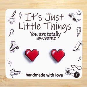 May include: A white card with the text "It's Just Little Things You are totally awesome" and two red pixel heart earrings. The card has various 8-bit style graphics around the text, including a skateboard, roller skates, and a game controller. The text "handmade with love" is at the bottom of the card.