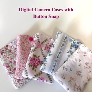 May include: Digital camera cases with button snap closure. The cases feature floral patterns in pink, purple, and blue. Each case has a different floral design and a button snap closure. The text "Digital Camera Cases with Button Snap" is visible.
