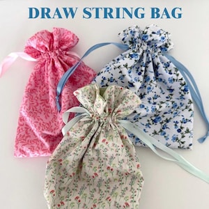 May include: Three drawstring bags in pink, floral, and blue patterns. Each bag has a ribbon drawstring. The text "DRAW STRING BAG" is at the top of the image. These bags are ideal for small gifts or storage.