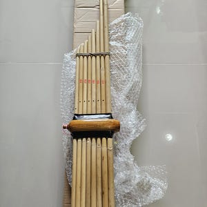 Op de afbeelding: Een traditioneel Thais muziekinstrument genaamd een Khlui, gemaakt van bamboe, met een mondstuk van hout en een reeks buizen van verschillende lengtes. Het instrument is omwikkeld met touw en verpakt in een kartonnen doos.