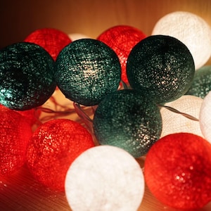 May include: A collection of illuminated string lights featuring red, white, and green woven spheres. The spheres are lit from within, creating a warm, inviting glow. Ideal for festive decor.