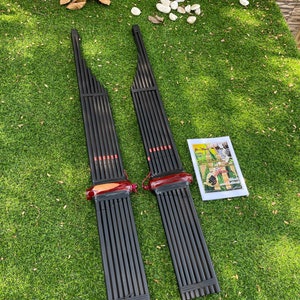 Puede incluir: Dos instrumentos musicales de madera negra con detalles rojos, colocados sobre hierba verde. Los instrumentos se llaman "Khene" y son órganos de boca tradicionales tailandeses.