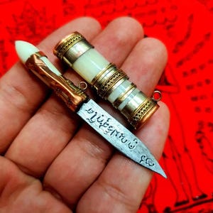 May include: A small, silver knife with a white and gold handle. The blade is engraved with Thai script. The knife is folded and fits inside a white and gold case.