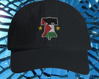 May include: Black baseball cap featuring an embroidered design of a bell in the colors of the Palestinian flag, with two gold stars on either side. The cap has a curved brim and a classic, adjustable fit.