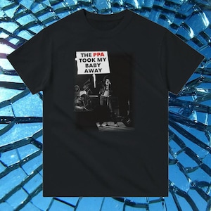 May include: Black t-shirt featuring a black and white image of a band performing on stage. The lead singer is holding a sign that reads "THE PPA TOOK MY BABY AWAY".