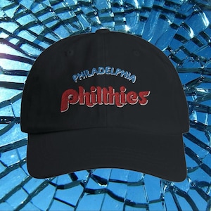 May include: Black baseball cap with a red and blue embroidered logo that says "PHILADELPHIA PHILLIES".