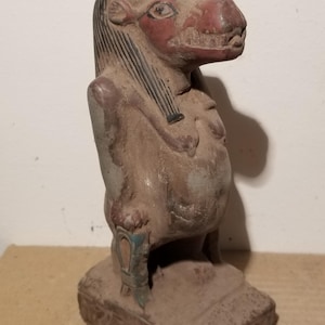 Peut inclure: Une statue égyptienne antique et usée représentant une divinité ressemblant à un hippopotame. La sculpture présente un museau rouge, des cheveux noirs et une base détaillée. La figurine est principalement marron avec des touches de bleu et de vert.