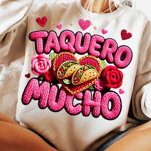 Puede incluir: Sudadera blanca con la frase "TAQUERO MUCHO" en rosa, con un dise&ntilde;o en forma de coraz&oacute;n con tacos, rosas y corazones. Incluye rodajas de lima y detalles dorados.