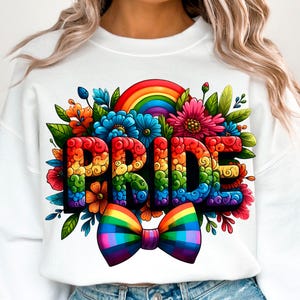 以下が含まれることがあります： レインボーカラーの「PRIDE」の文字が特徴の白いスウェットシャツ。カラフルな花、虹、虹色の蝶ネクタイで囲まれています。このデザインは鮮やかで、LGBTQ+のプライドを祝っています。