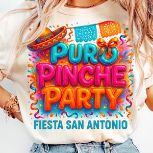 May include: A white t-shirt with a colorful graphic design that says "Puro Pinche Party Fiesta San Antonio". The graphic features a sombrero, confetti, and colorful streamers.