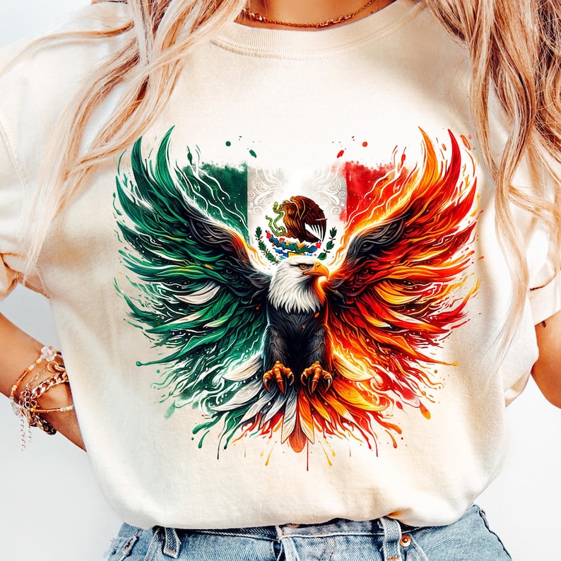 May include: A white t-shirt with a graphic of a stylized eagle with its wings spread wide. The eagle is depicted with a green, white, and red color scheme, reminiscent of the Mexican flag. The eagle is holding a snake in its talons.