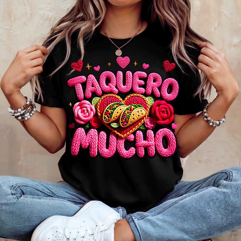 Puede incluir: Camiseta negra con las palabras "TAQUERO MUCHO" en rosa, con un dise&ntilde;o en forma de coraz&oacute;n con dos tacos. El dise&ntilde;o incluye rosas y corazones rosas. Una prenda informal.